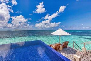 Maldives luxury beach resort. Infinity swimming pool, beach chairs or loungers under umbrellas in over water villa. Blue sky, amazing lagoon. Summer holiday, travel vacation. Outdoor tourism landscape photo