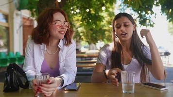 två kvinnor sitta på utomhus- Kafé tabell talande och nickar video