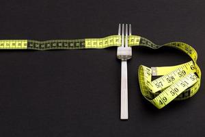 Fork with a measuring tape on a black background, diet or healthy eating concept photo