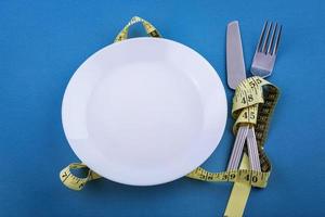 White plate on a blue background, measuring tape with a fork and knife photo