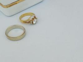 un par de anillos de boda y anillos de compromiso hechos de oro amarillo y paladio con accesorios en forma de caja de anillo blanca con una lista de oro y un espacio vacío para completar el texto foto