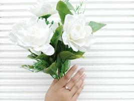 una joven de indonesia con un anillo de bodas en el dedo medio y sosteniendo una flor blanca con hojas verdes. con un fondo blanco foto