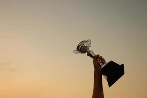 Victory concept with a hand holding a trophy on the sunset sky background photo