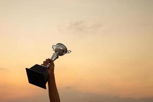 Victory concept with a hand holding a trophy on the sunset sky background photo