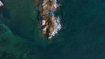 Beautiful vertical aerial view of blue waves breaking over a rockey shoreline at video