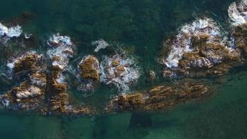 Beautiful vertical aerial view of blue waves breaking over a rockey shoreline at video