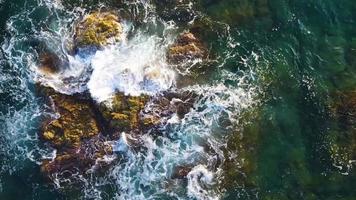 skön vertikal antenn se av blå vågor brytning över en stenig strandlinje på video