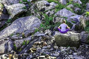 joven rubia de atrás sentada en una piedra y meditando en las montañas. mujer por detrás. silencio mental foto