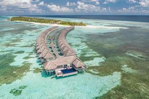 vista aérea de la isla de maldivas, resort de lujosas villas acuáticas y muelle de madera. hermoso cielo y fondo de la playa de la laguna oceánica. concepto de vacaciones y viajes de vacaciones de verano. paraíso aéreo paisaje pano
