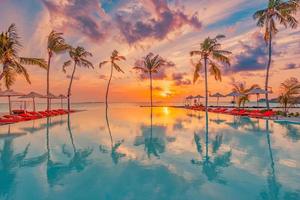 puesta de sol tropical sobre la piscina infinita al aire libre en el balneario de verano, paisaje de playa. lujosas vacaciones tranquilas en la playa, reflexión junto a la piscina, relajante chaise lounge romántico cielo colorido, sillas sombrilla foto