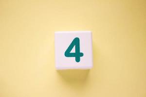 Close-up photo of a white plastic cube with a green number 4 on a yellow background. Object in the center of the photo