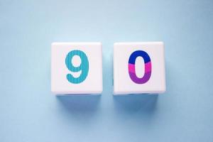 Close-up photo of a white plastic cubes with a colorful number 90 on a blue background. Object in the center of the photo