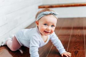 pequeña niña gateando de un año sentada en el suelo con luz brillante en la sala de estar cerca de la ventana sonriendo y riendo foto