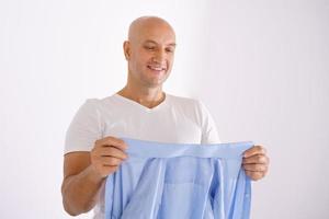 A bald man holding a clean shirt on a white background photo