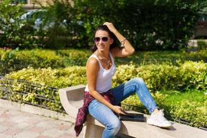 Outdoors portrait glamorous young brunette woman with glasses sitting on bench photo