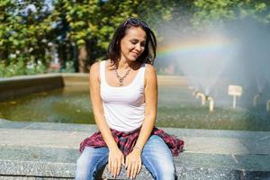 hermosa mujer feliz sentada cerca de la fuente. chica en ropa casual en verano foto