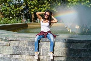 Cheerful young brunette woman against background fountain happy shows gesture photo