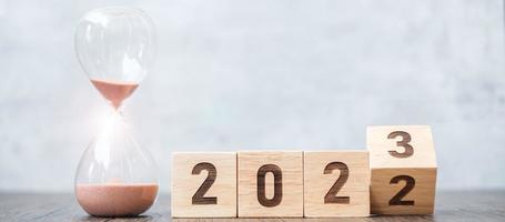 flip block 2022 a 2023 texto con reloj de arena en la mesa. resolución, tiempo, plan, objetivo, motivación, reinicio, cuenta regresiva y conceptos de vacaciones de año nuevo foto