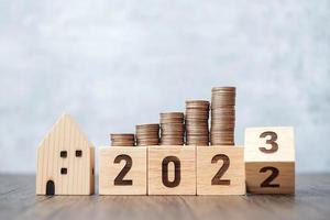 2022 flipping to 2023 year block with house model and Coins stack. real estate, Home loan, tax, investment, mortgage, financial, savings and New Year Resolution concepts photo