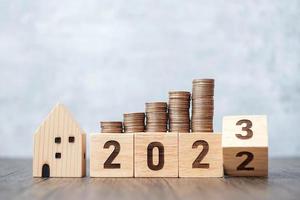 2022 pasando al bloque de 2023 años con modelo de casa y pila de monedas. conceptos inmobiliarios, hipotecarios, fiscales, de inversión, hipotecarios, financieros, de ahorro y de resolución de año nuevo foto