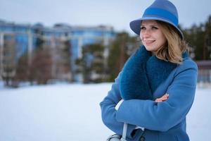 Beautiful woman in blue coat and hat posing outdoors in the snow photo