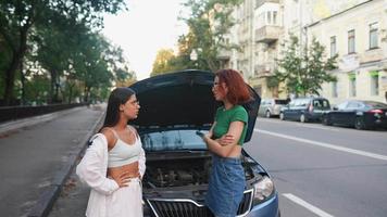 deux jeunes femmes regardent sous le capot d'une voiture video