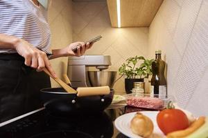 mujer cocinando salsa boloñesa y usando smartphone foto