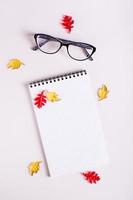 Autumn still life empty notepad, glasses and colored leaves on a pink background. Top and vertical photo