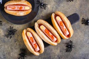 Halloween recipe for hot dogs with sausage fingers in ketchup on a slate on the table. Top view photo