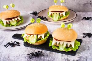 hamburguesas monstruosas caseras con ojos y lengua para el menú de halloween en pizarra y arañas en la mesa foto