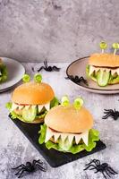 Homemade monster burgers with eyes and tongue for halloween menu on slate and spiders. Vertical view
