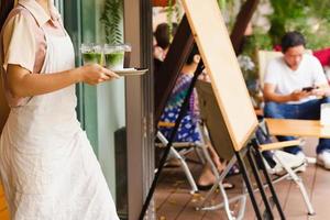 Waitress with apron serving iced matcha latte to customer at cafe photo