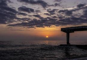 paisaje marino al atardecer con cielo nublado, puesta de sol y muelle foto