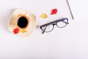 Autumn still life cup of black coffee, glasses and colored leaves on a pink background. Top view. photo