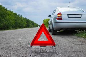 señal roja de parada de emergencia y coche plateado roto en la carretera foto