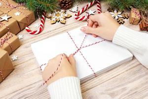 Many envelopes tied with rope. Close-up top view of famale hands with envelope. Pine cones and christmas decoration on old wooden table, desk photo