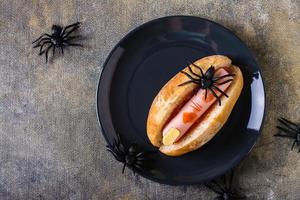 An amputated sausage finger in ketchup in a bun on a plate. Halloween recipe. Top view photo