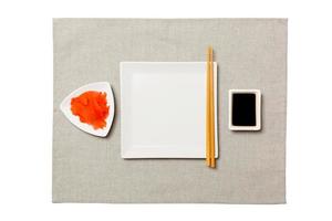 Empty white square plate with chopsticks for sushi, ginger and soy sauce on grey napkin background. Top view with copy space for you design photo