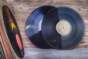 A pile of old vinyl records stand on a shelf against the background of a wooden wall photo