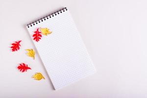 Autumn still life blank notepad and colored leaves on a pink background. Top view. photo