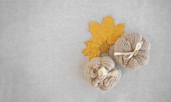 Hobby background with handmade knit pumpkins and golden maple leaves. DIY, craft decoration for fall and winter holidays. Flat lay, top view photo