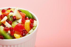 Bowl with fruit salad on a pink background. Juicy and ripe fruit slices. photo