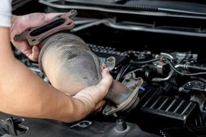 Close up old catalytic converter in hand Technician remove from engine gasoline car dust clogged condition on filter in service concept photo