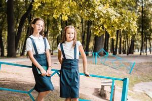 Two pupils in school uniform stand near the fence in the park on a warm day photo