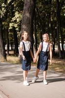 Two elementary pupils smile and hold hands and go to school on a warm day. Vertical view photo