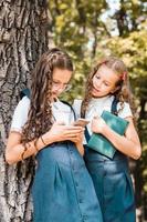 Classmates in school uniform with a book looking at a smartphone day in the park. Vertical view photo