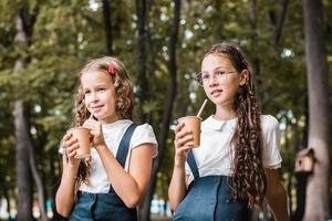 dos colegialas están bebiendo de tazas ecológicas y bebiendo pajitas en el parque foto