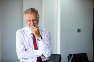 anciano hombre de negocios de pie con confianza sonriendo y riendo feliz en la sala de reuniones foto