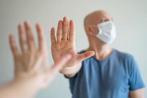 A bald man holds a medical mask in his hands, his other hand held out in protest photo