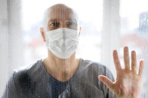 portrait of a man in a protective mask looks through the windows to the street photo